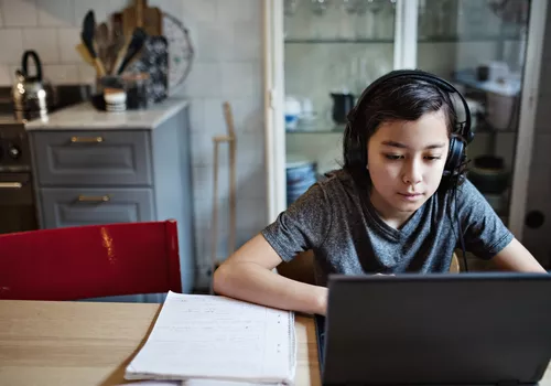 Evde ödev sırasında dizüstü bilgisayar kullanırken kulaklık takan çocuk